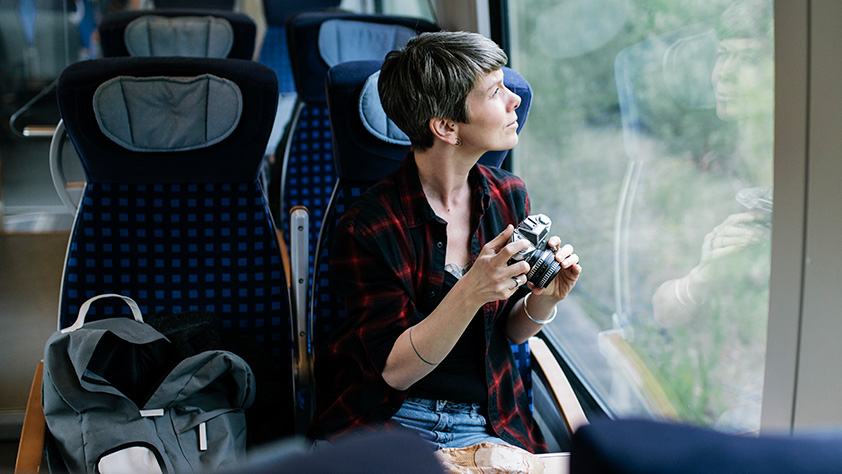 An older female backpacker enjoying the scenery and taking photos during a train journey