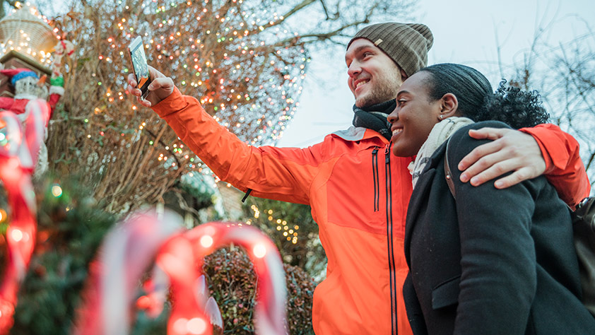 5 U.S. Towns Wrapped in Holiday Spirit - Couple Taking a Selfie in Front of a Holiday Lights Display