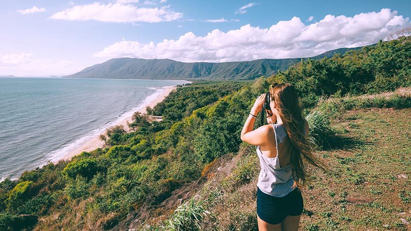 Woman looking out over the water through a camera at Rex Lookout on the highway between Cairns and Port Douglas, Australia