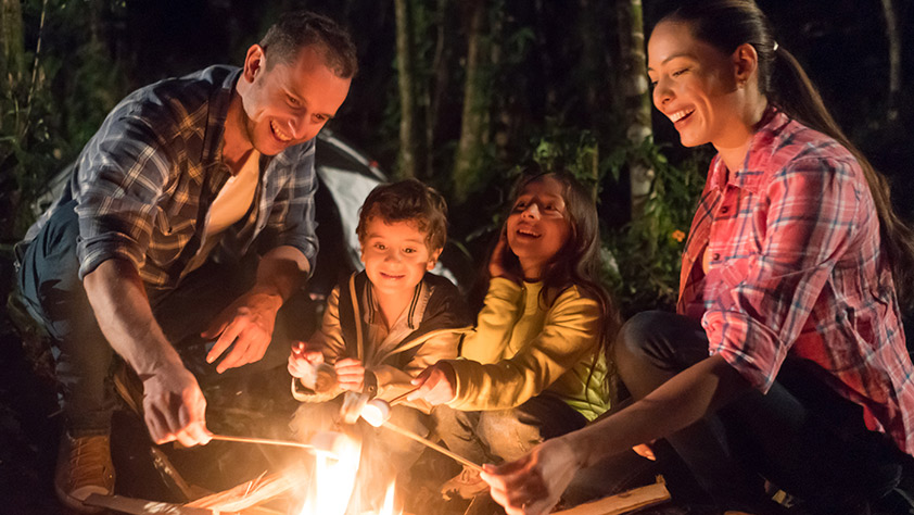 Happy family eating marshmallows by a bonfire