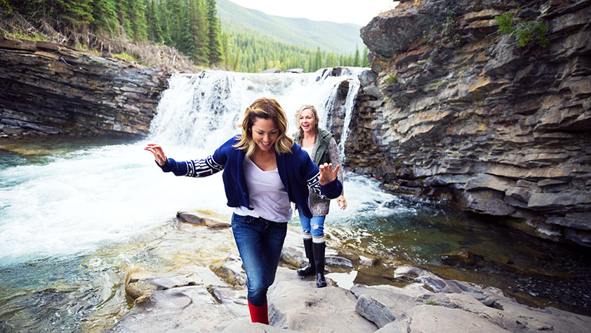 Two women climbing rocks near a waterfall