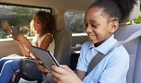 Two Happy Children Sitting in a Car Reading From Tablets