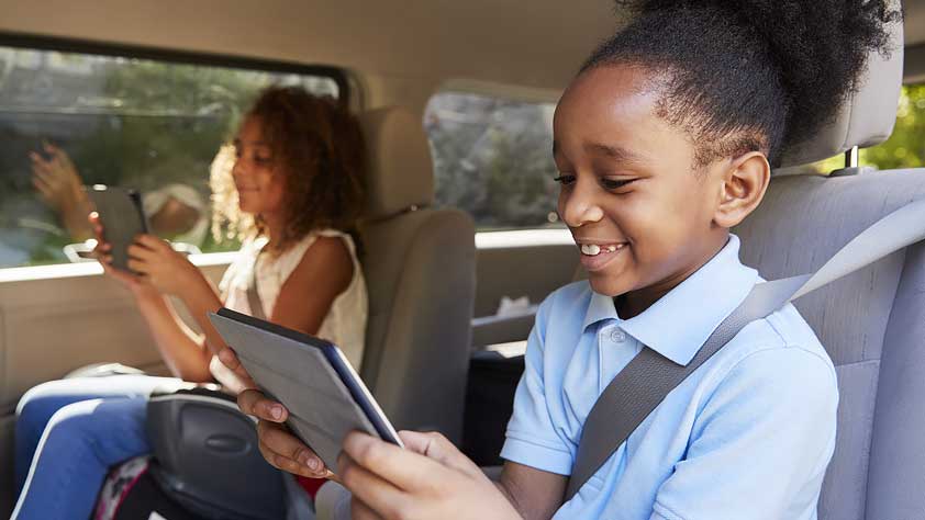 Easy Ways to Keep Your Kids Happy on a Family Vacation - Two Children Sitting in a Car Reading From Tablets