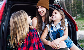 Mother and Daughters Laughing and Sitting in the Trunk of a Hatchback Car 