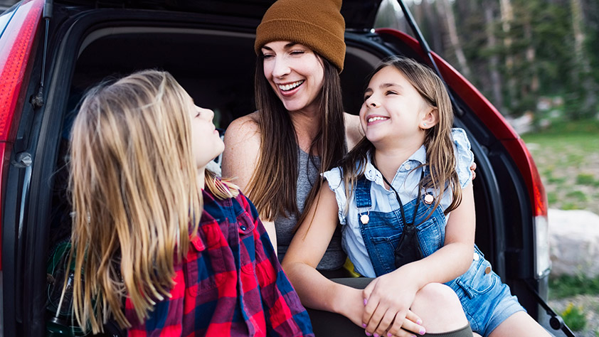 Mother and Daughters Laughing and Sitting in the Trunk of a Hatchback Car 