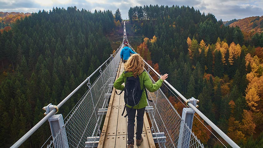 Hikers Walking Across a Forest Bridge in Fall - Fall Vacation Ideas