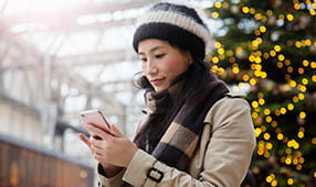 Woman on Smartphone Standing in Front of Christmas Tree Display