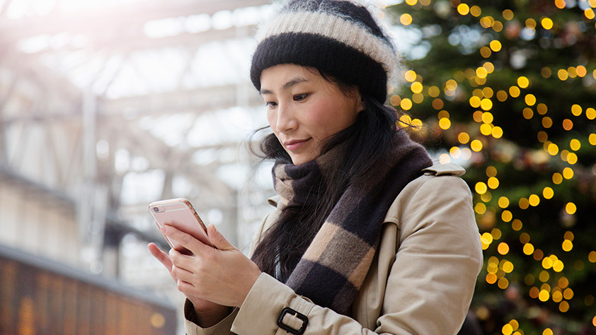Woman on Smartphone Standing in Front of Christmas Tree Display