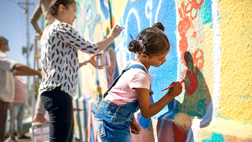 Girl volunteers painting a vibrant mural on a sunny wall