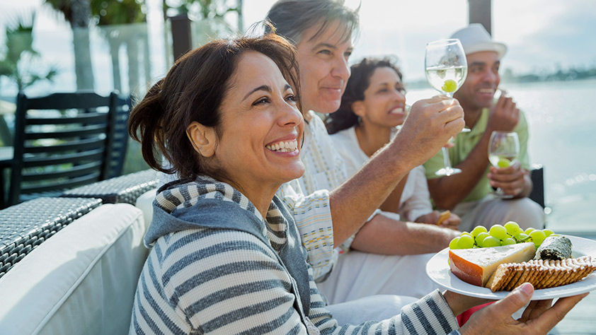 Smiling woman holding a cheese plate with friends on a patio