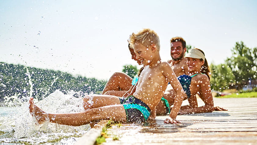 Playful siblings sitting on a lake pier with their parents on a sunny day