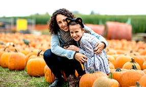Mother and daughter sit on pumpkins at a pumpkin farm