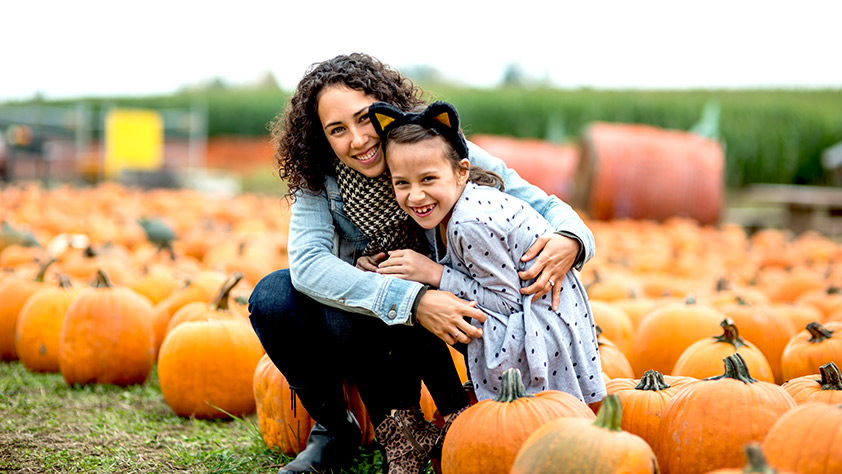 Mother and daughter sit on pumpkins at a pumpkin farm