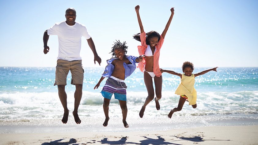 An Excited Family of Four Jumping Into the Air on the Beach