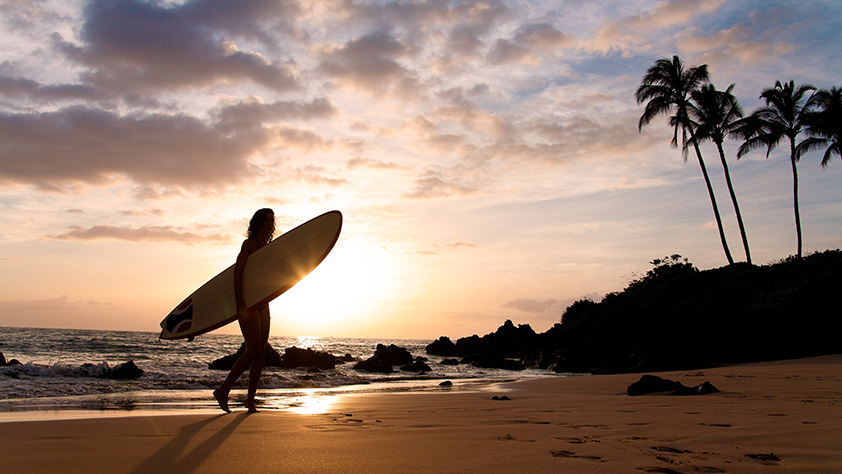 Silhouette of a female surfer at sunset on tropical beach