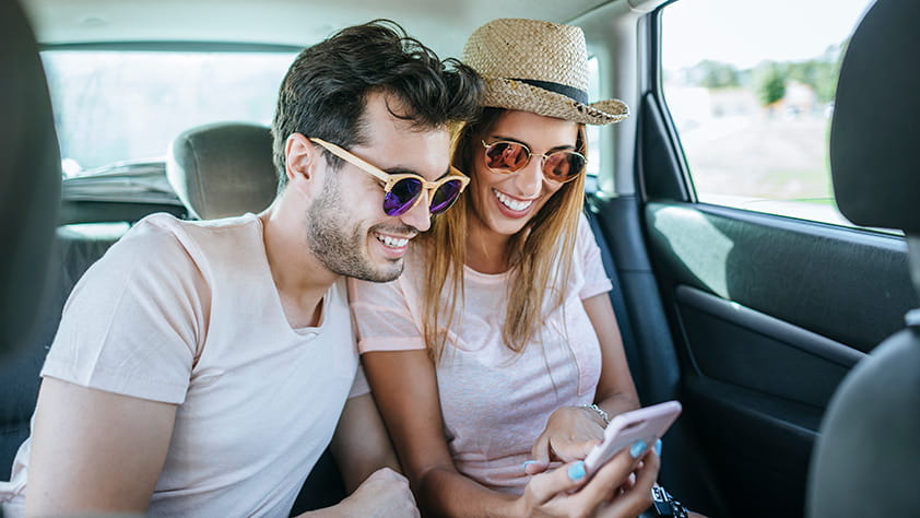 Couple in the back seat of a car looking at a cell phone