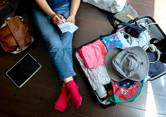 Woman sitting on the floor with her open suitcase writing in a notepad