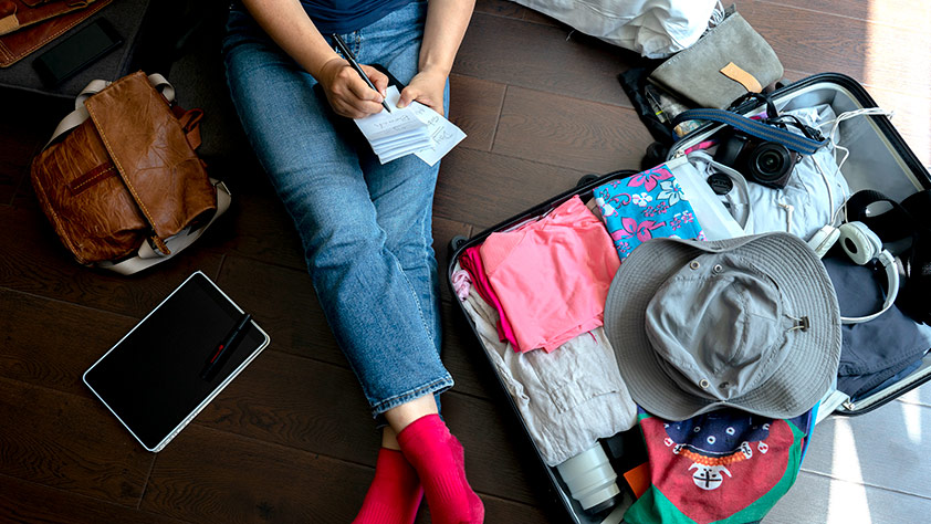 Woman sitting on the floor with her open suitcase writing in a notepad