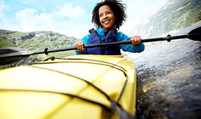 Woman in a blue jacket and life vest paddling a bright yellow kayak