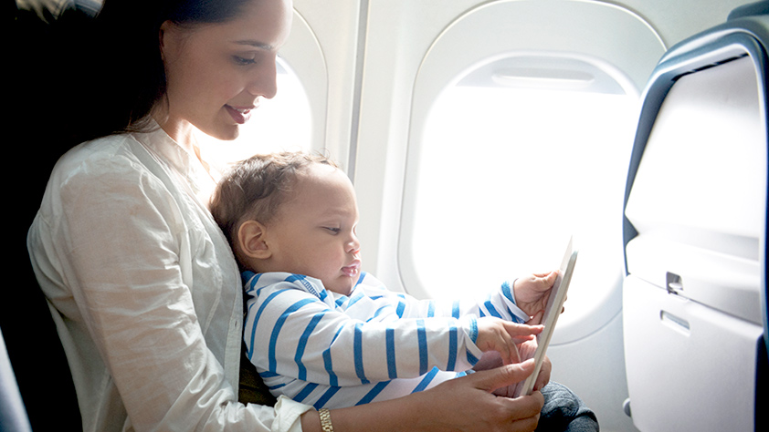 Mother and toddler son sitting in an airplane using a digital tablet