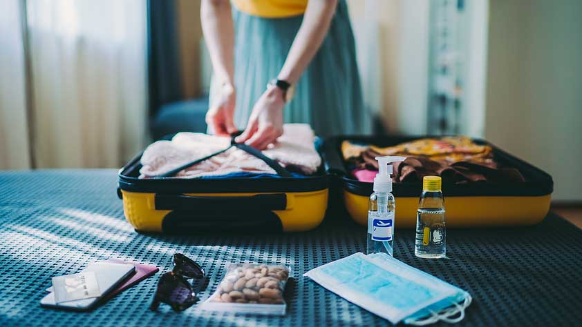Woman Packing Suitcase for a Trip Including Face Masks and Hand Sanitizer