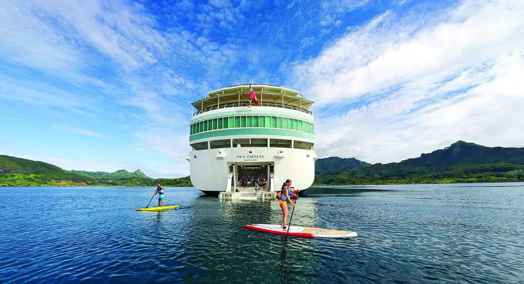 Two tourists paddleboarding in front of a cruise ship
