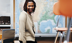 African-American teacher sitting on a desk in her classroom