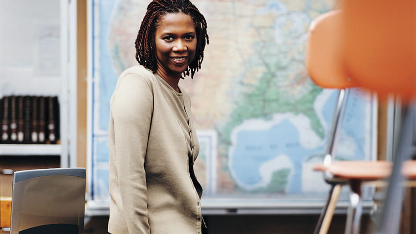 African-American teacher sitting on a desk in her classroom