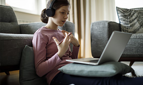 Teenage Girl with Headphones and Laptop Having Online School Class at Home