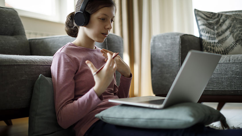Teenage Girl with Headphones and Laptop Having Online School Class at Home