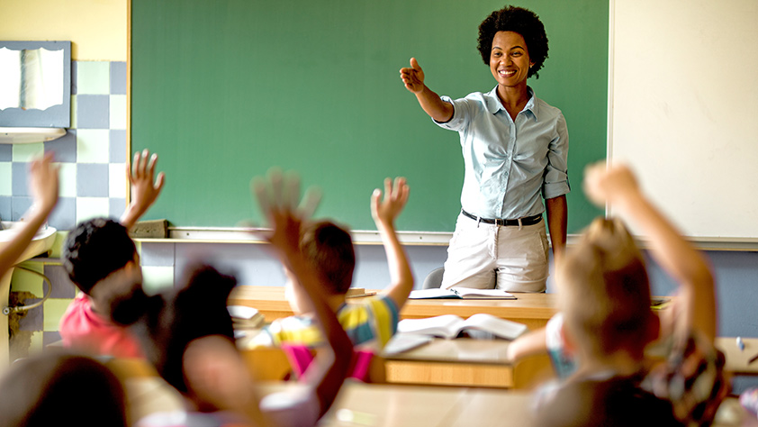 Happy African-American elementary teacher asking questions to her class