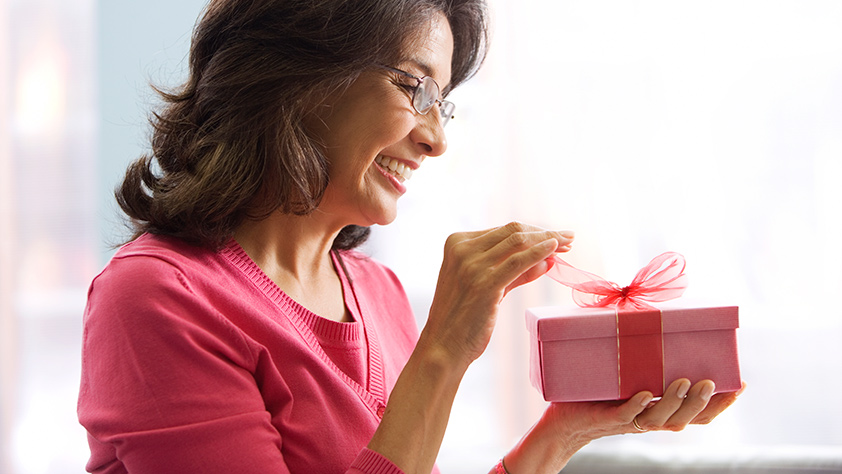 Woman in a red shirt opening a present wrapped with a red bow