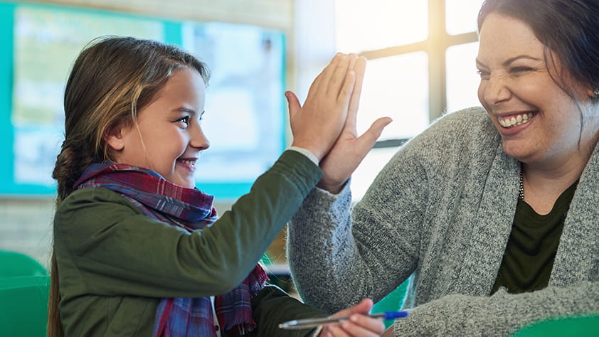 An elementary school girl high-fiving her teacher in class
