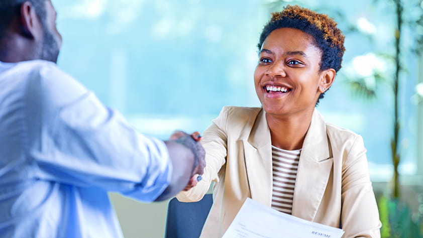Confident young woman at a job interview, holding her resume and shaking hands with the interviewer