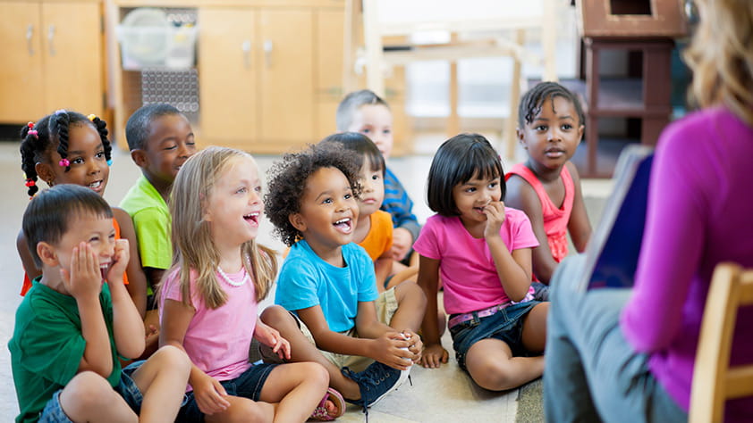 Preschool children sitting on the classroom floor for story time with their teacher