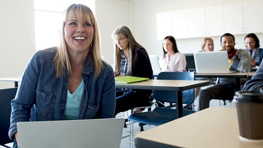 Smiling adult education student using a laptop in a classroom
