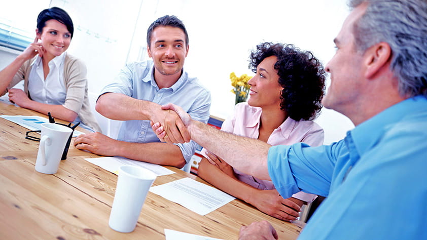 A smiling candidate shaking hands with a potential coworker in a group interview