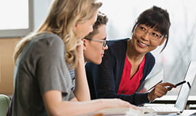 Teacher and high school students working at a laptop