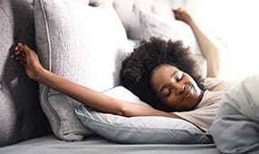Happy young woman waking up in her bed at home and stretching her arms above her head