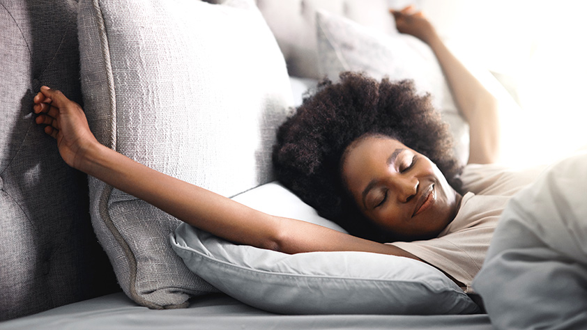 Happy young woman waking up in her bed at home and stretching her arms above her head