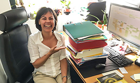 Woman Laughing In Front of Large Stack of Papers on Desk