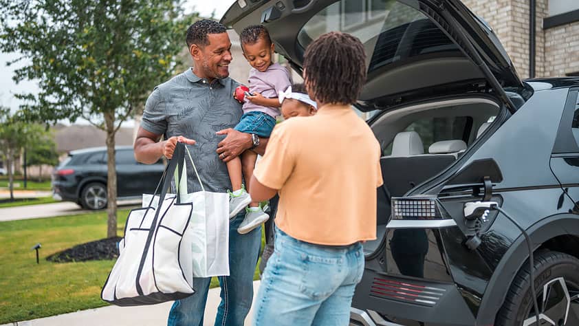 A happy family unloads groceries from their car in front of their home