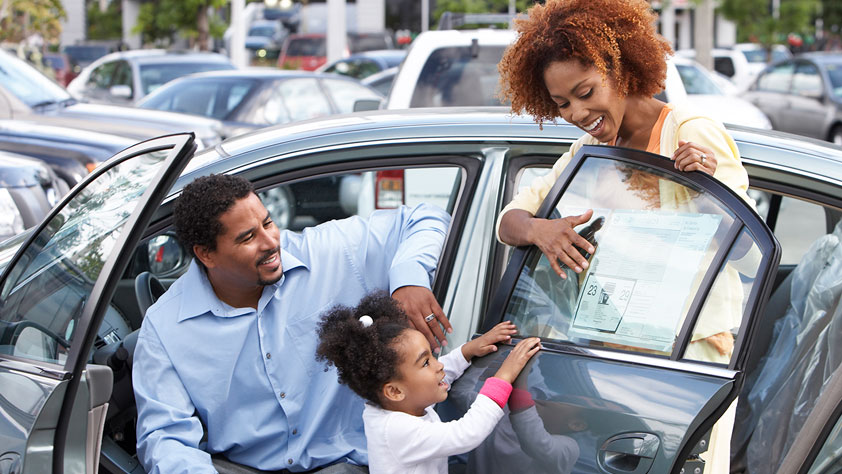 African-American family looking at stats on the window sticker of a new car