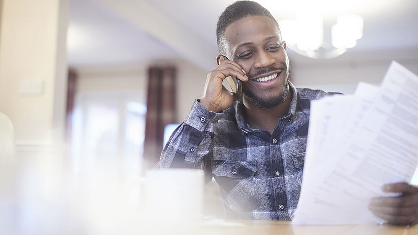 how to Get and Compare Car Insurance Quotes - Young Man on the Phone at Home Holding Paperwork