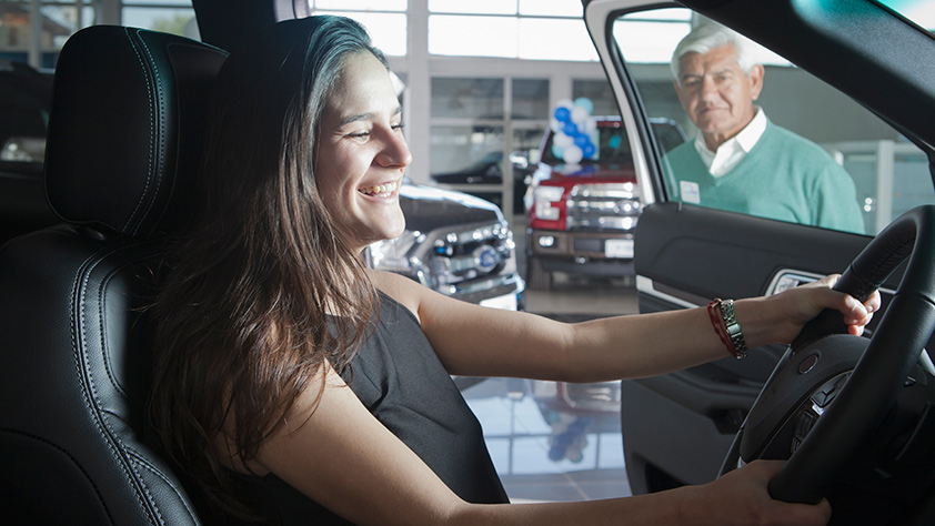 Happy young women sitting behind the wheel of a car at a car dealership