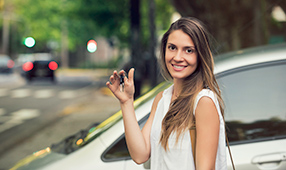 Young woman standing outside next to a car holding a key
