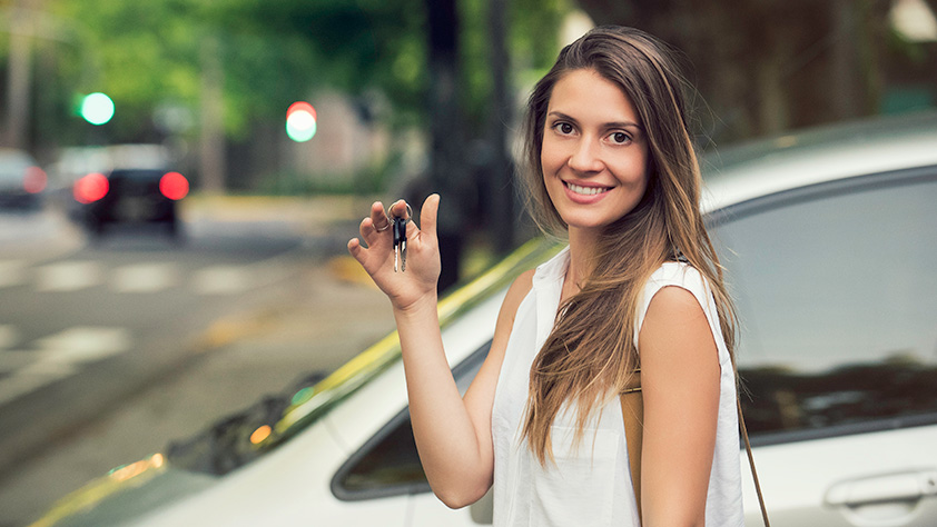 Young woman standing outside next to a car holding a key