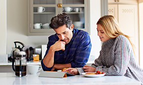 Young couple using a digital tablet while sitting at their kitchen table at home