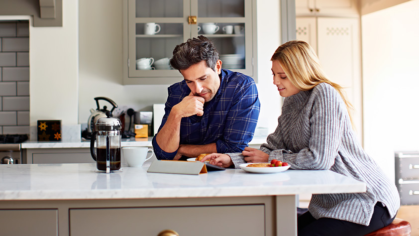 Young couple using a digital tablet while sitting at their kitchen table at home