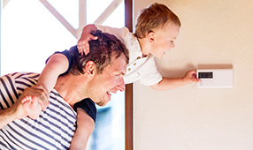 Father Carrying Son on Shoulders, Adjusting Thermostat